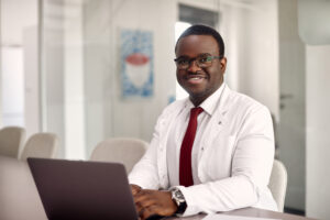 Happy African American Doctor Working On Laptop And The Clinic And Looking At Camera. - ADF PRO